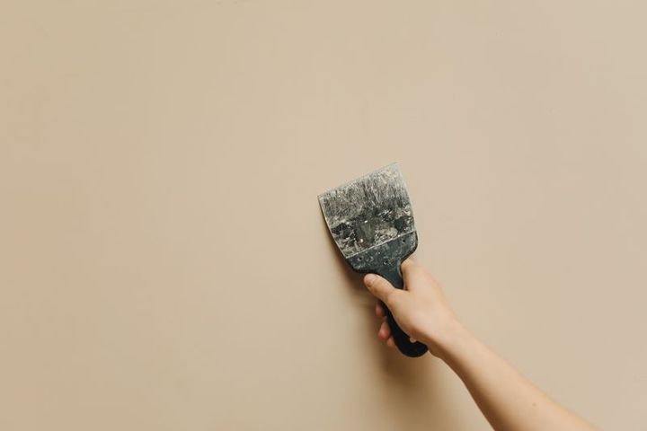 A hand applying a drywall patch with a putty knife