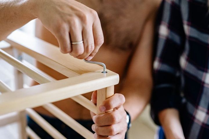 Hands assembling wooden furniture with an Allen key